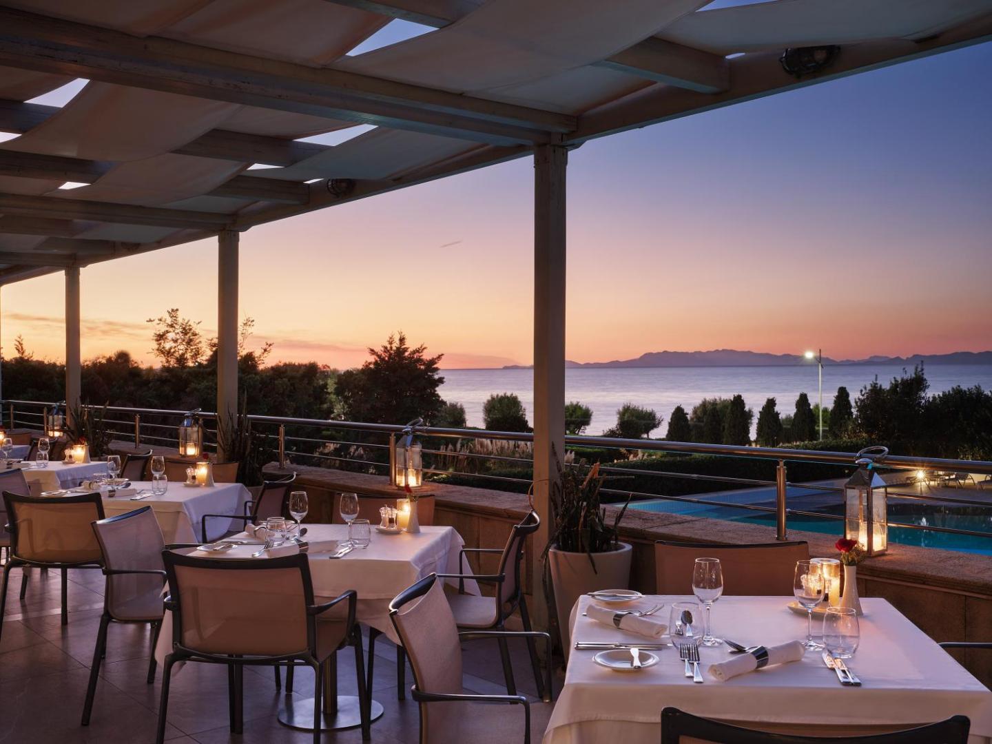 Amus Hotel & Spa eleganta āra terase vakarā ar balti klātiem galdiem, laternām un skatu uz baseinu un jūru