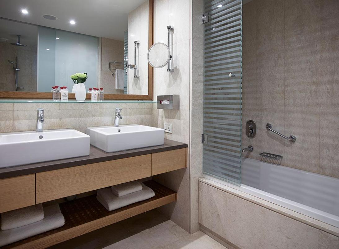 Amus Hotel & Spa numura vannas istaba ar divām izlietnēm, lielu spoguli un vannu gaišos toņos
