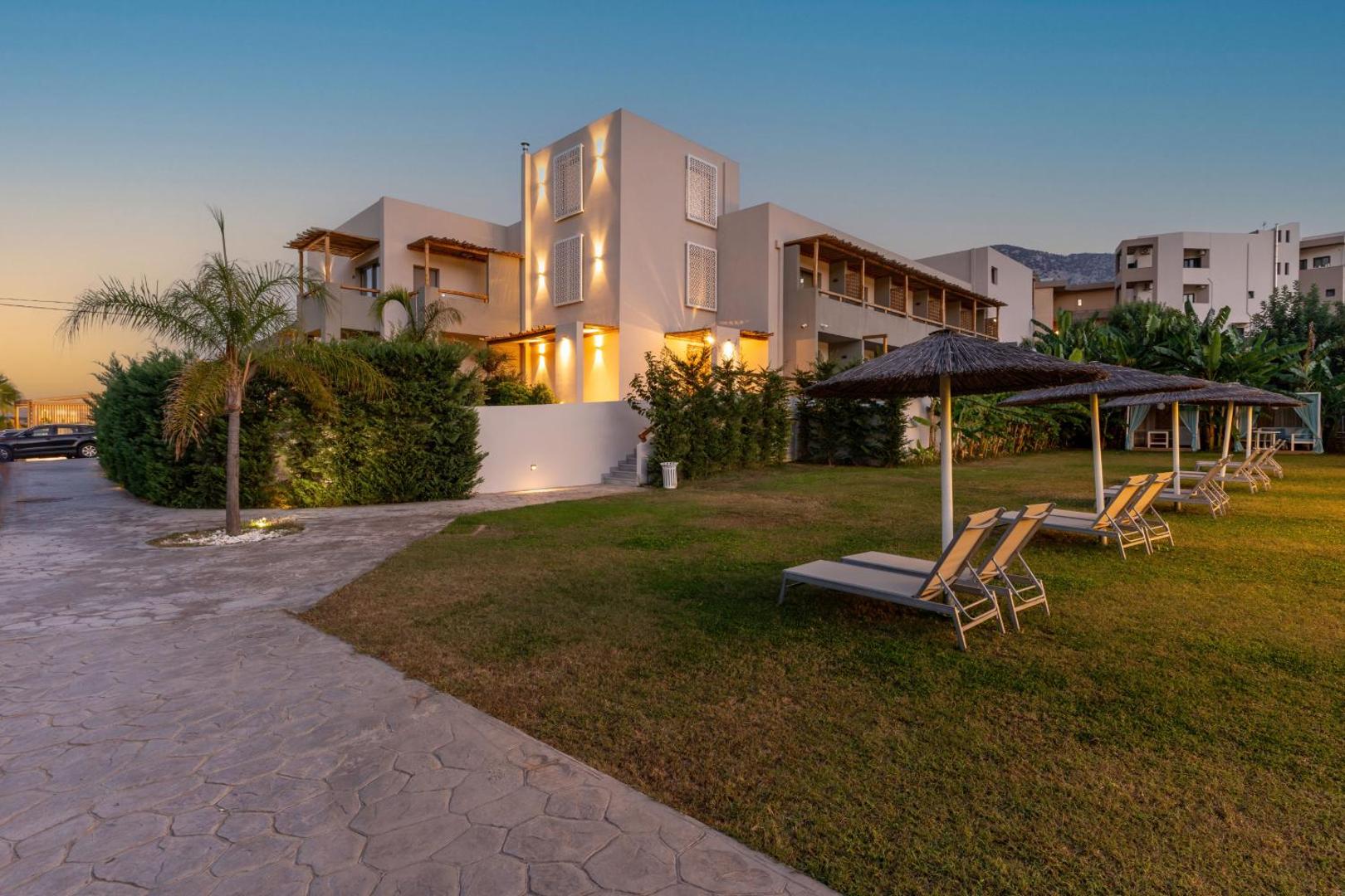 Bali Star Resort Hotel dārza zona ar zālāju un guļamkrēsliem zem saulessargiem vakara saulē — skats uz viesnīcas fasādi