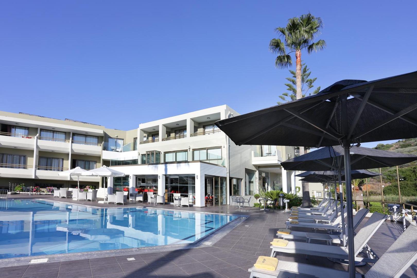Bali Star Resort Hotel galvenais baseins ar sauļošanās krēsliem un bāru piekrastē Krētā — moderna arhitektūra un palmas
