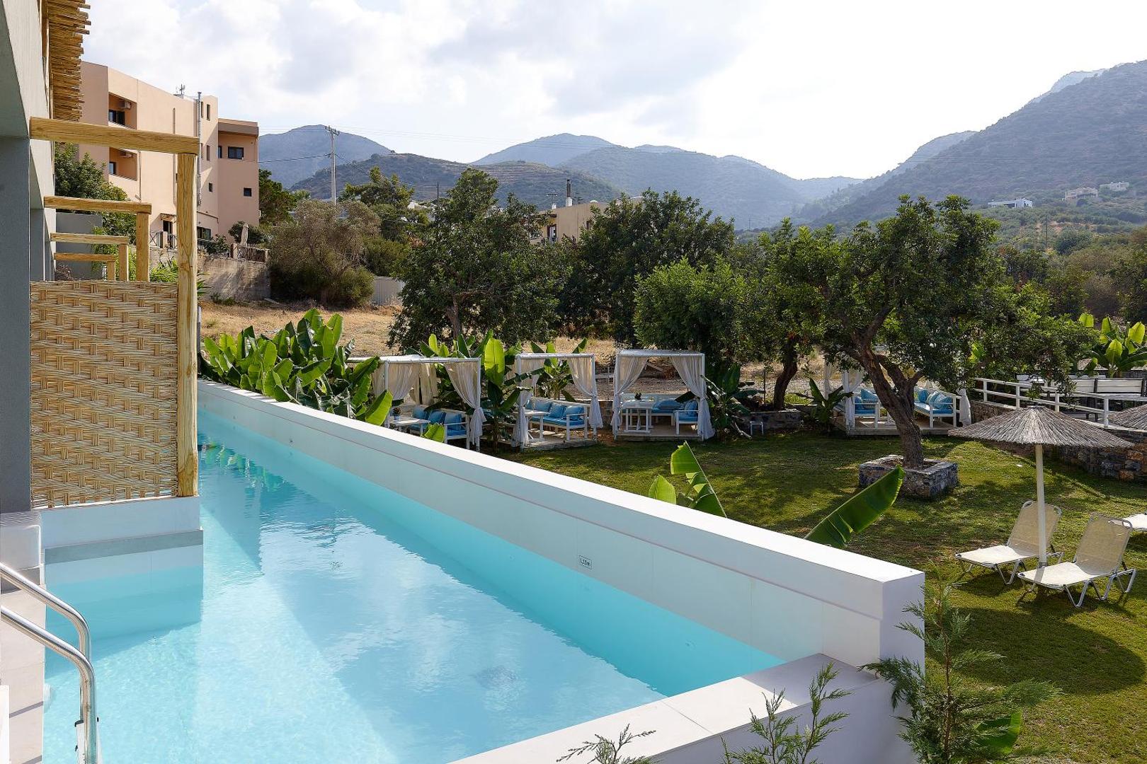 Bali Star Resort Hotel koplietošanas baseins ar skatu uz dārzu un kalniem Krētā — atpūtas nojumes un sauļošanās krēsli zālienā