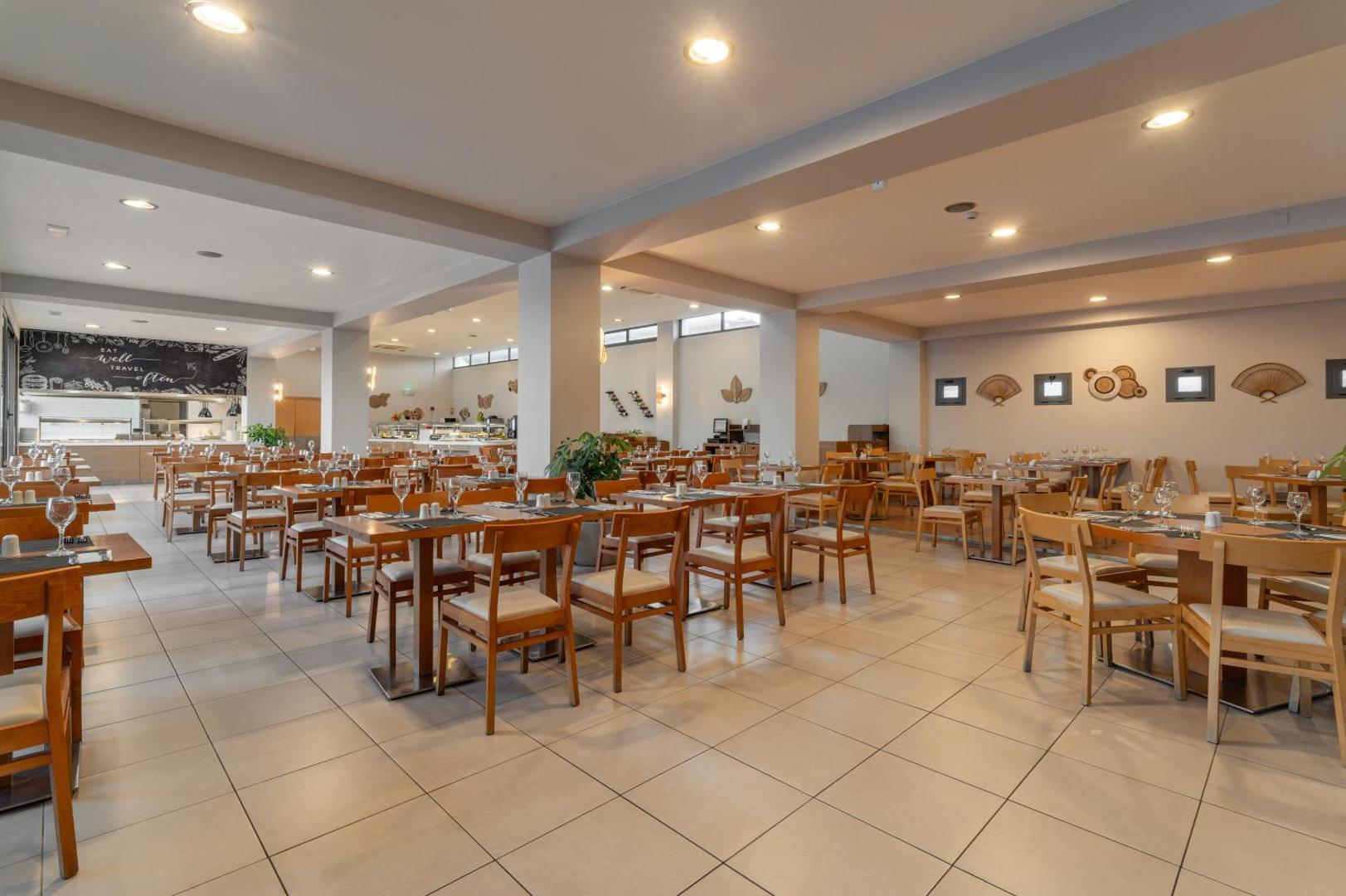 Plašs Ariadne Beach Hotel restorāns ar daudziem galdiem un krēsliem Malijā — skats uz bufetes līniju un dekoratīvām sienām