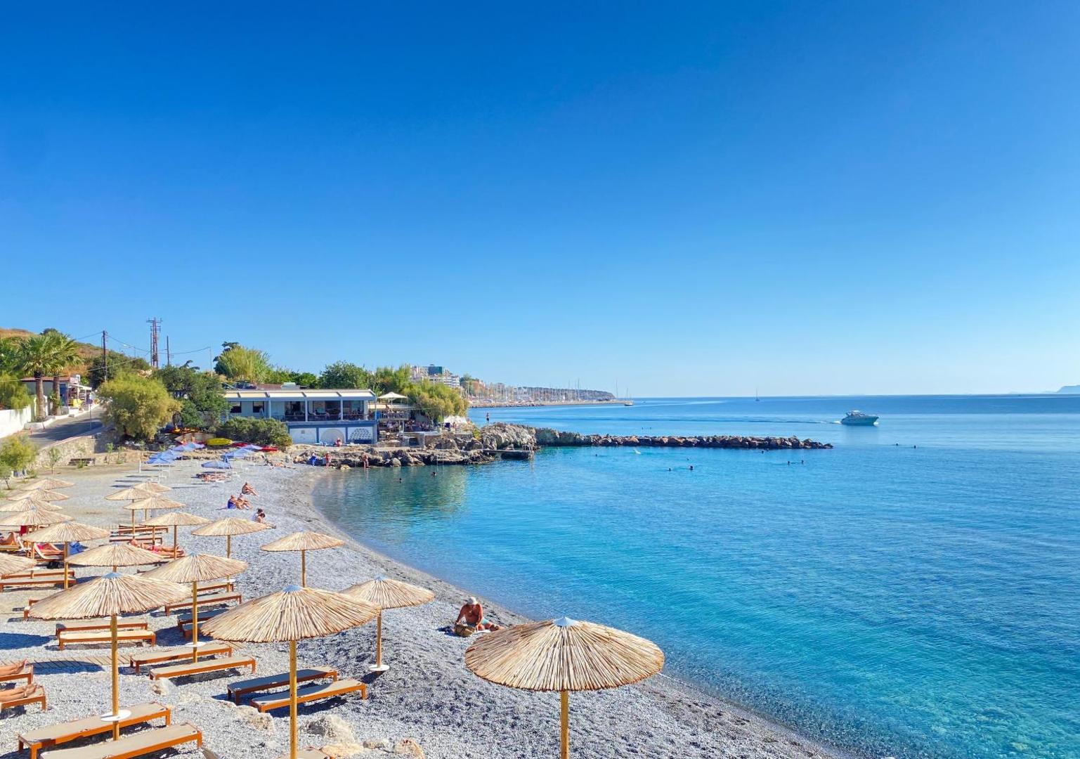 Ariadne Beach Hotel Malia oļu pludmale Krētā ar salmu saulessargiem un zviļņiem pie dzidri zila jūras līča saulainā dienā