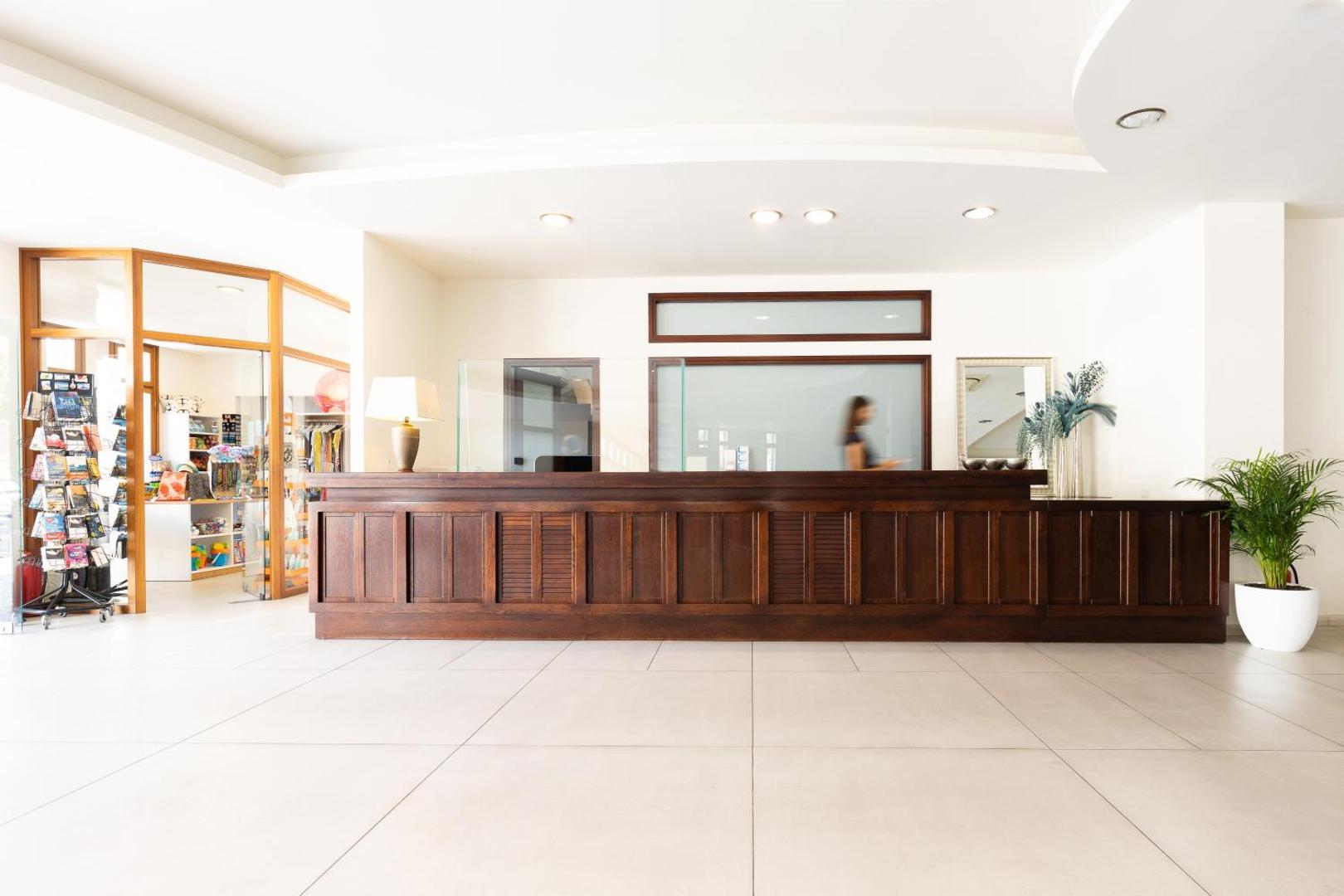 Ariadne Beach Hotel Malia gaišā recepcijas zona ar tumša koka reģistrācijas leti un suvenīru veikalu blakus Malijā, Krētā