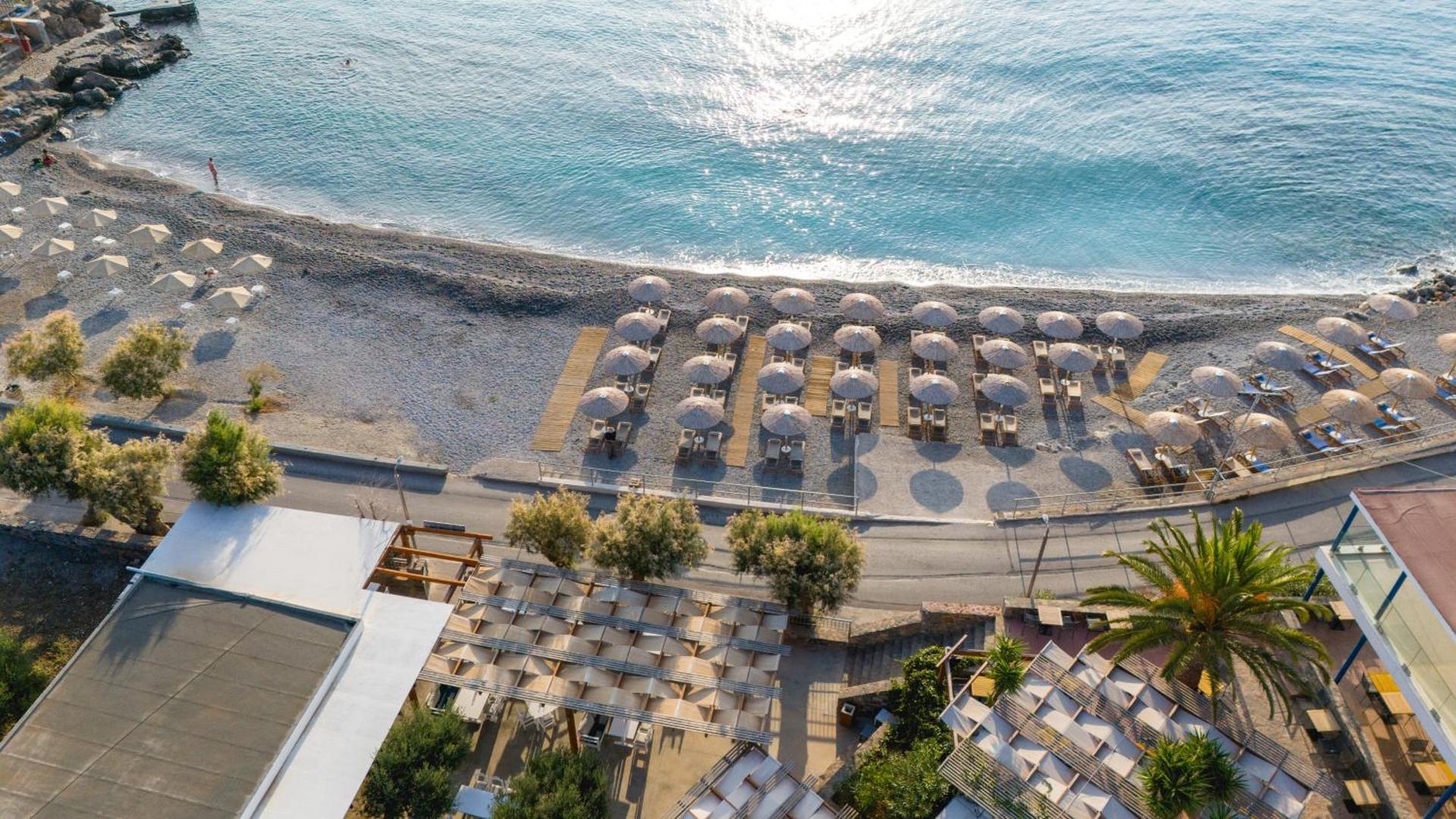 Ariadne Beach Hotel Malia skats no augšas uz pludmales zonu, terasēm un saulessargu rindām piekrastes joslā saulrieta gaismā