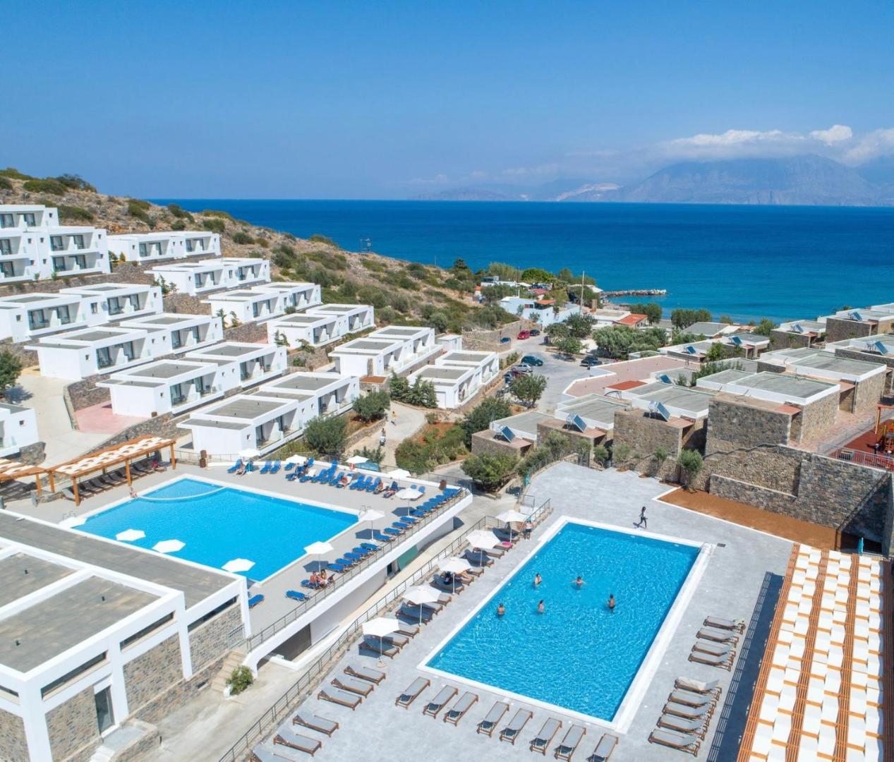 Ariadne Beach Hotel panorāmas skats Malijā, Krētā — divi āra baseini, sauļošanās terase un balti numuru korpusi piekrastē ar skatu uz jūru