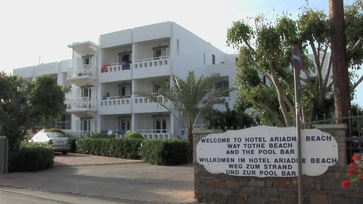 Ariadne Beach Hotel norādes zīme pie iebrauktuves Malijā — balta ēka ar balkoniem un informāciju par ceļu uz pludmali