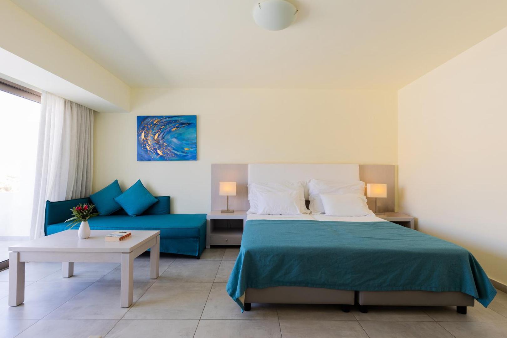 Ariadne Beach Hotel gaišs numurs ar divguļamo gultu, zilu dīvānu un kafijas galdiņu Malijā, Krētā — minimālistisks dizains ar mākslas darbu pie sienas.