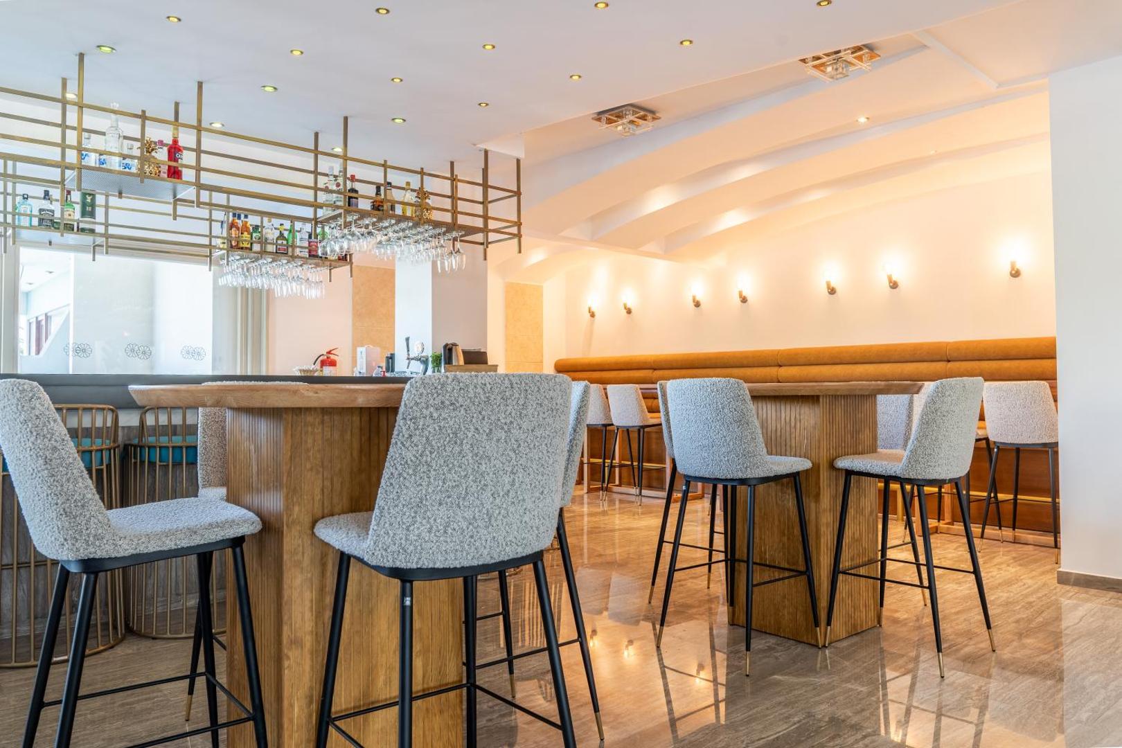 May Hotel bāra zona ar augstajiem krēsliem, koka galdiem un modernu apgaismojumu mājīgai vakara atpūtai