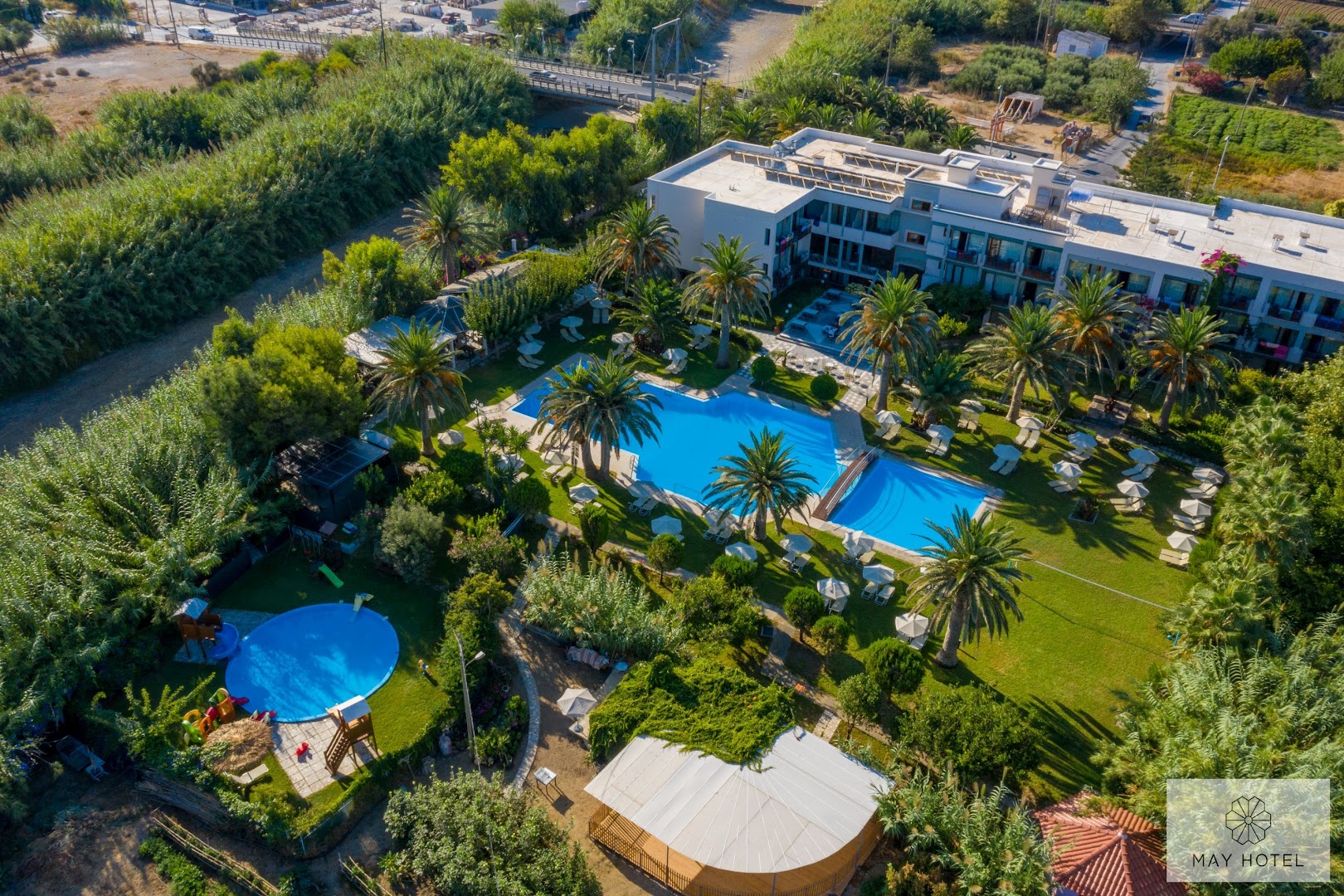 May Beach Hotel viesnīcas ēka un baseinu komplekss no putna lidojuma Retimno reģionā — plašs dārzs un apkārtējā ainava