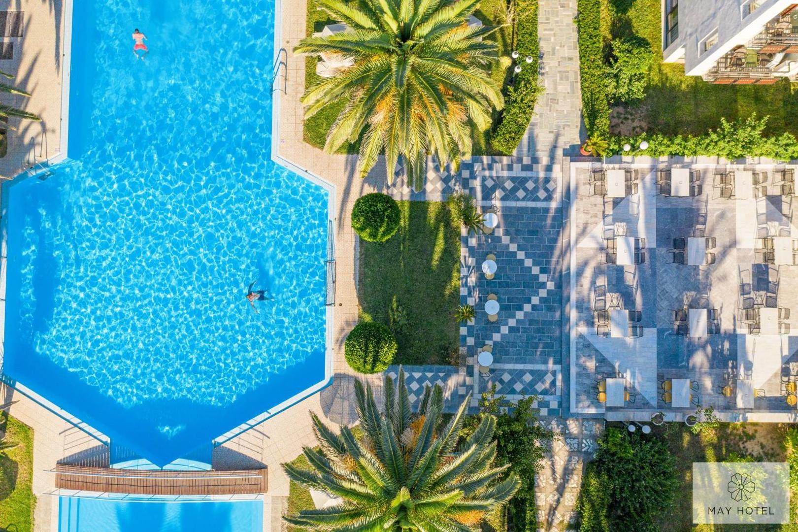 May Hotel skats no putna lidojuma uz zilo āra baseinu, palmu dārzu un āra terasi ar galdiņiem Retimno, Krētā.