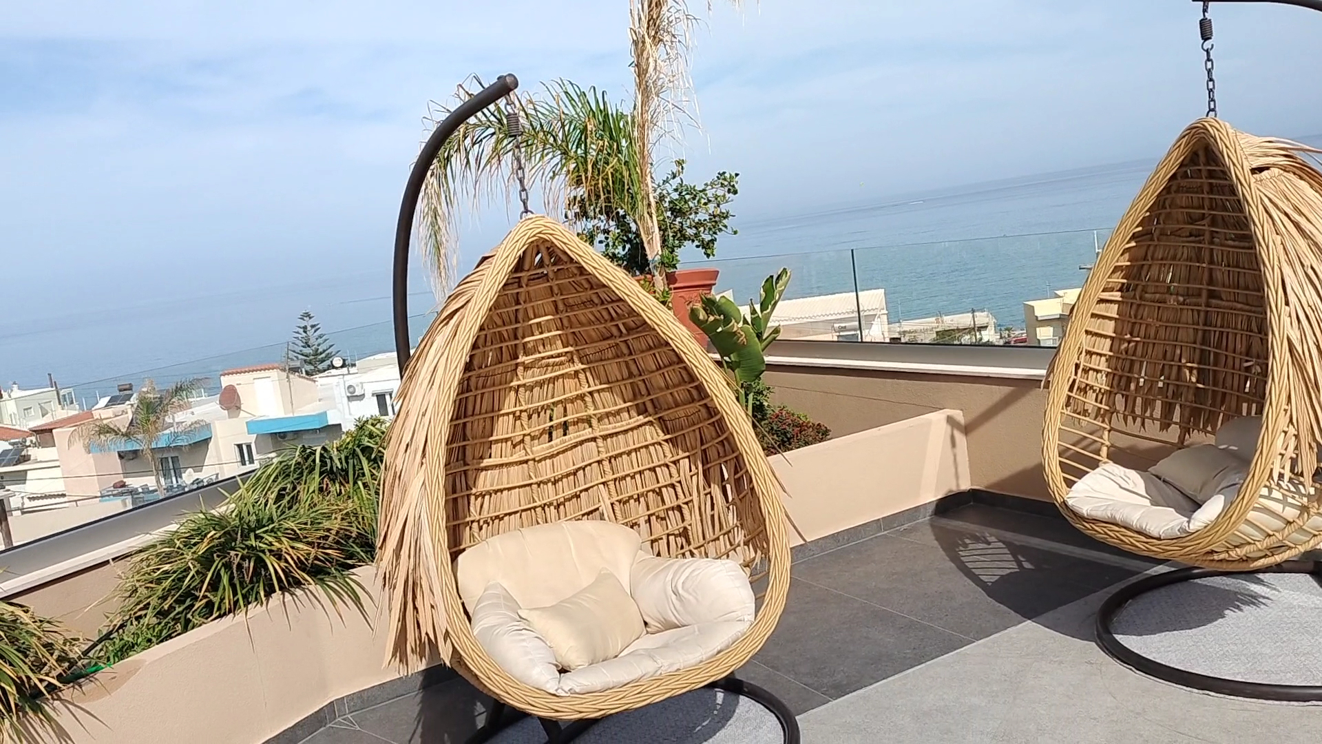 Minos Ambassador Suites & Spa atpūtas zona uz terases ar pītiem piekaramajiem krēsliem un skatu uz Vidusjūru