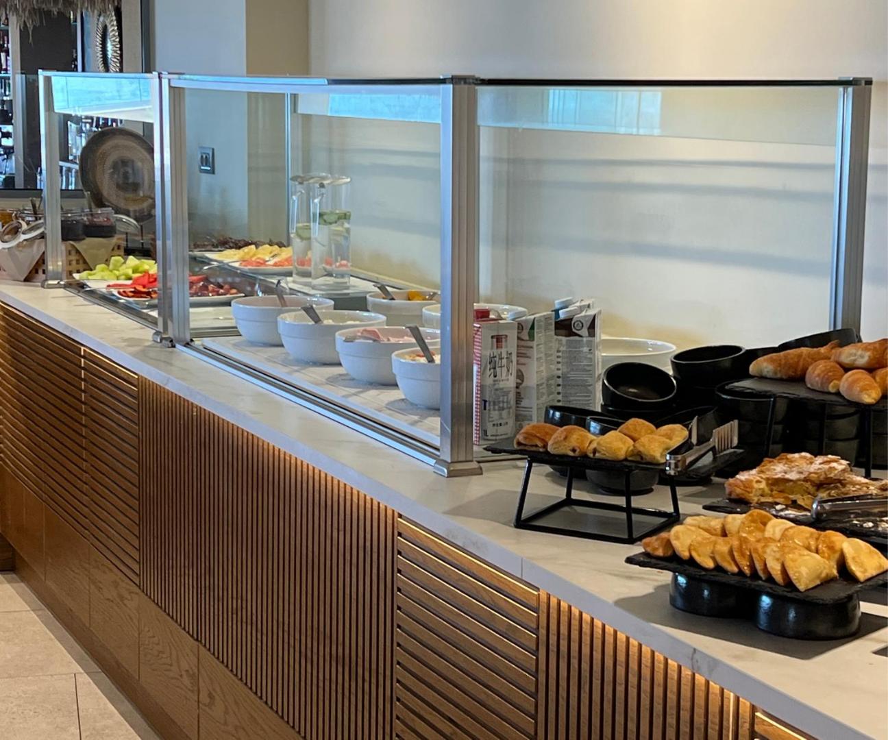 Minos Ambassador Suites & Spa brokastu bufete ar svaigiem augļiem, smalkmaizītēm un jogurtiem — daudzveidīga starptautiska virtuve viesnīcas restorānā