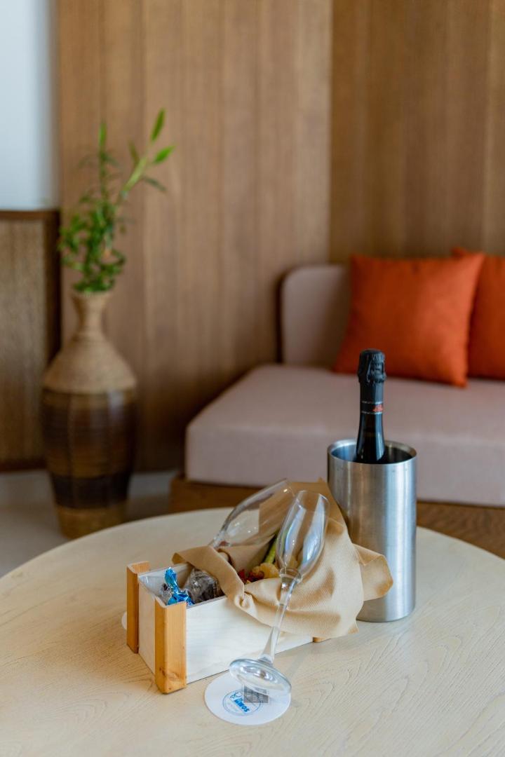 Viesu sagaidīšanas komplekts Minos Ambassador Suites & Spa numurā — dzirkstošais vīns un uzkodas uz koka galdiņa
