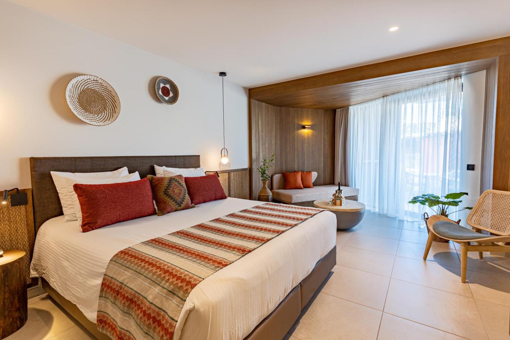 Gaišs un moderns Minos Ambassador Suites & Spa viesnīcas numurs ar lielu gultu, koka elementiem un boho stila dekorācijām