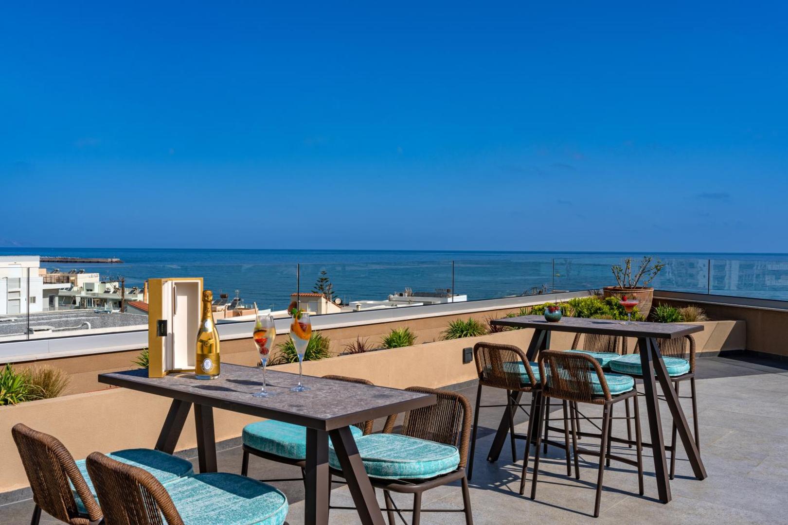 Minos Ambassador Suites & Spa jumta terase ar galdiem un skatu uz jūru Retimno, Krētā — saulains laiks un dzērieni