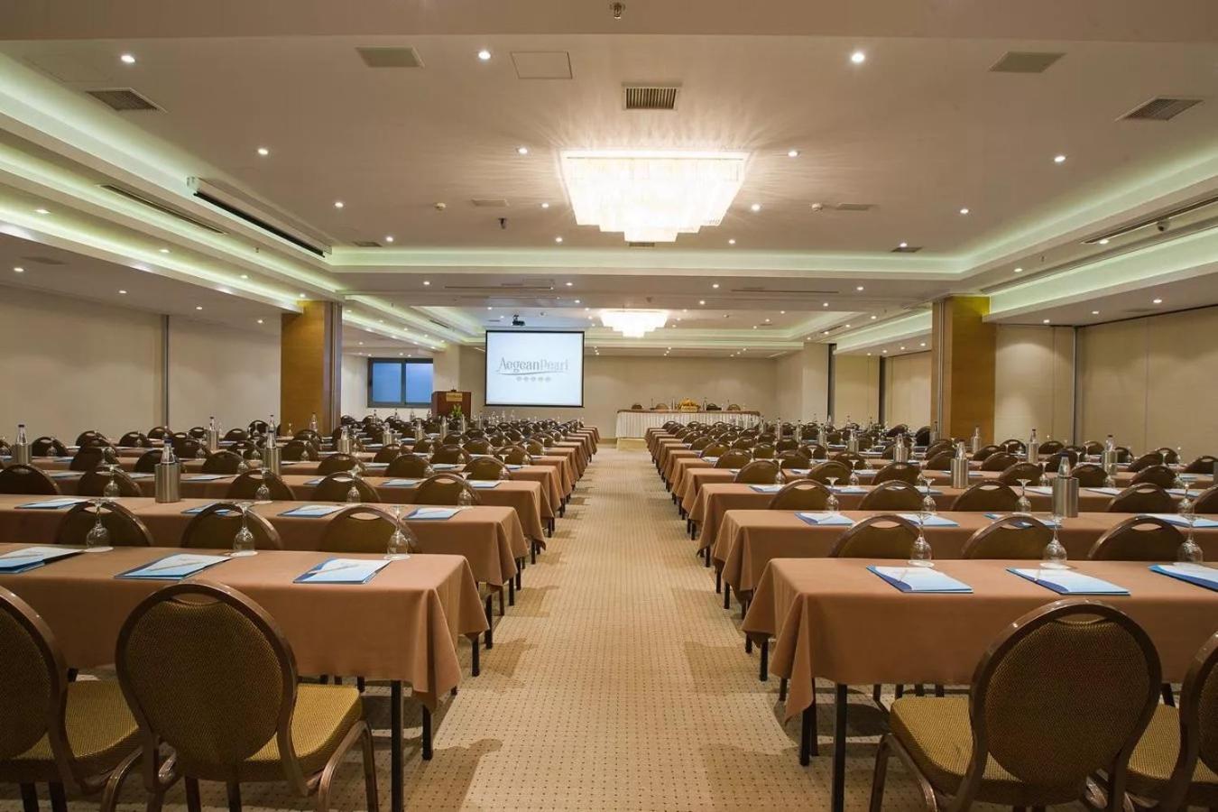 Plaša un moderna Aegean Pearl konferenču zāle ar daudzām sēdvietām, galdiem un prezentāciju aprīkojumu biznesa pasākumiem