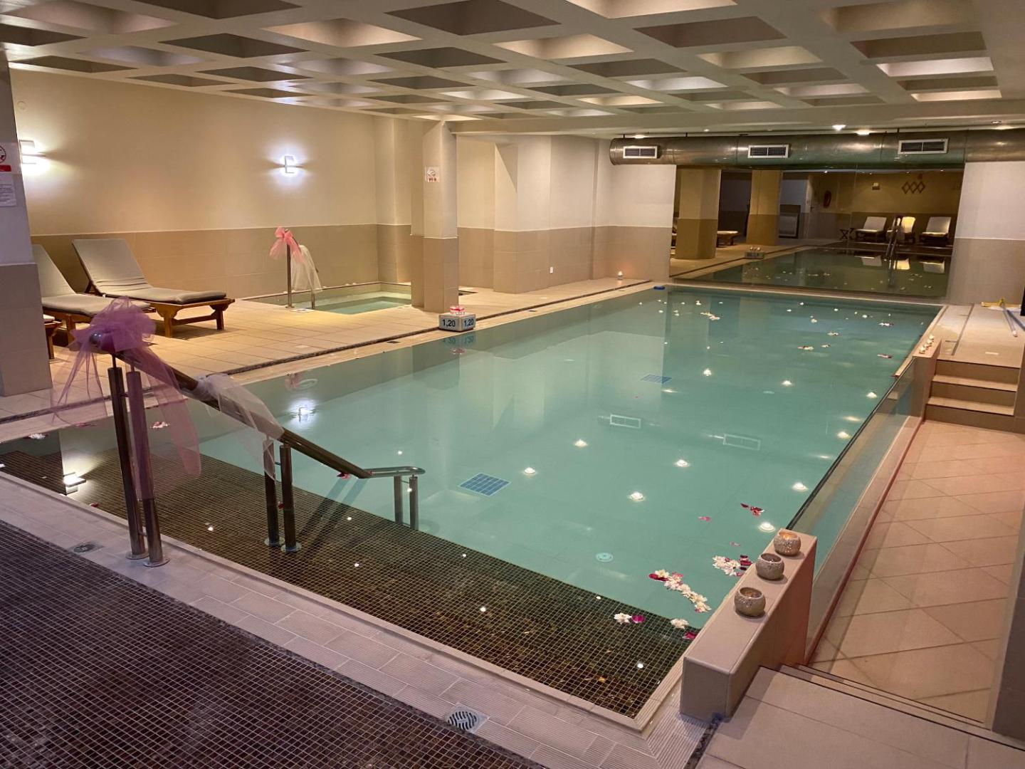 Aegean Pearl spa centra iekštelpu baseins ar siltu apgaismojumu, atpūtas krēsliem un dekoratīvām svecēm relaksējošai atpūtai