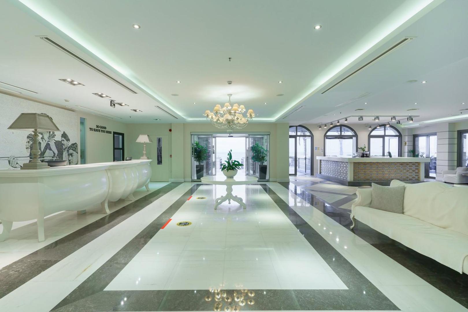 Aegean Pearl viesnīcas lobby un recepcijas zona ar baltām mēbelēm, greznu lustru un marmora grīdu