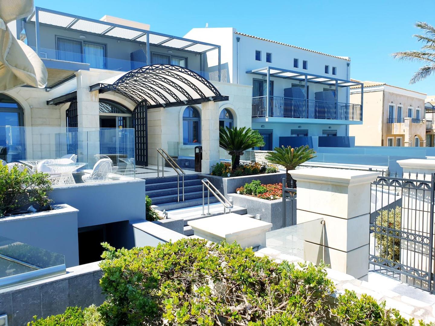 Sentido Aegean Pearl modernā arhitektūra ar stikla balkoniem, koptiem dārziem un atpūtas zonu pie ieejas