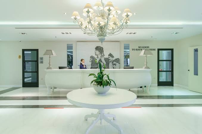 Aegean Pearl viesnīcas recepcijas zona Retimno, Krētā — elegants balts interjers ar greznu lustru, mākslas darbu un viesmīlīgu personālu