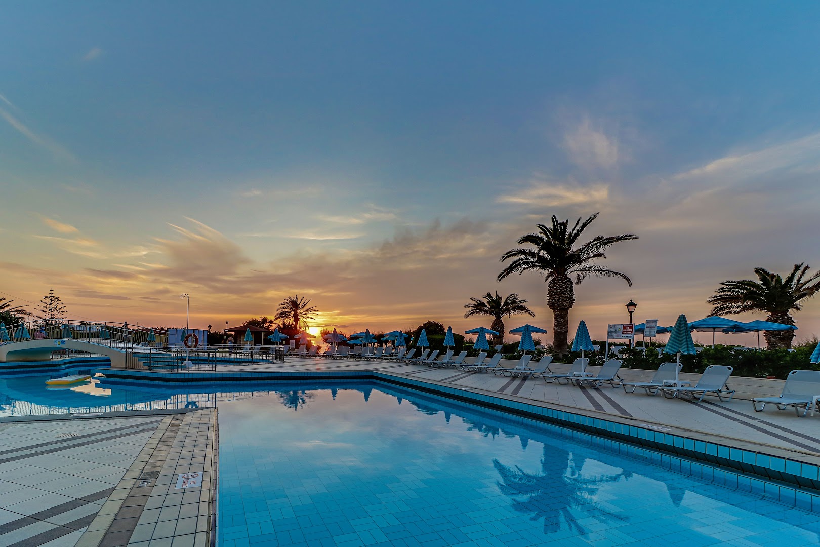 Creta Star Hotel baseina zona krēslas stundā ar izgaismotu ūdeni, sauļošanās krēsliem un palmām pie jūras
