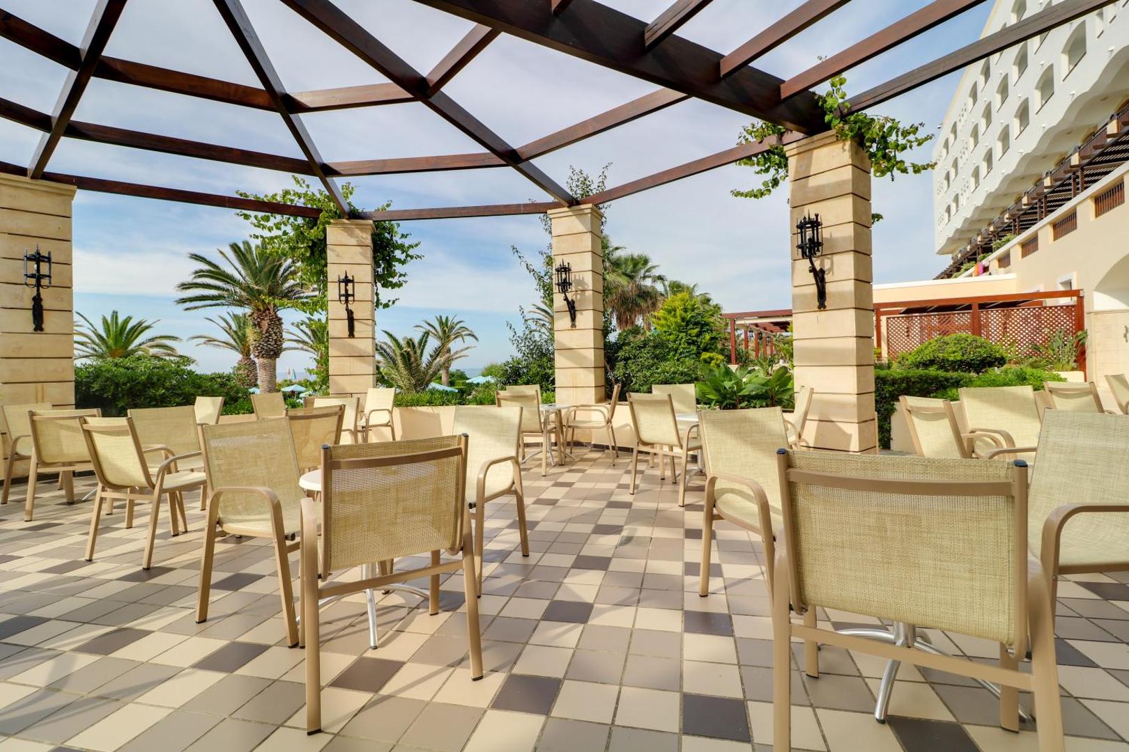 Creta Star Hotel āra atpūtas terase ar modernām mēbelēm zem koka pergolas, ko ieskauj zaļumi un palmas Krētā.