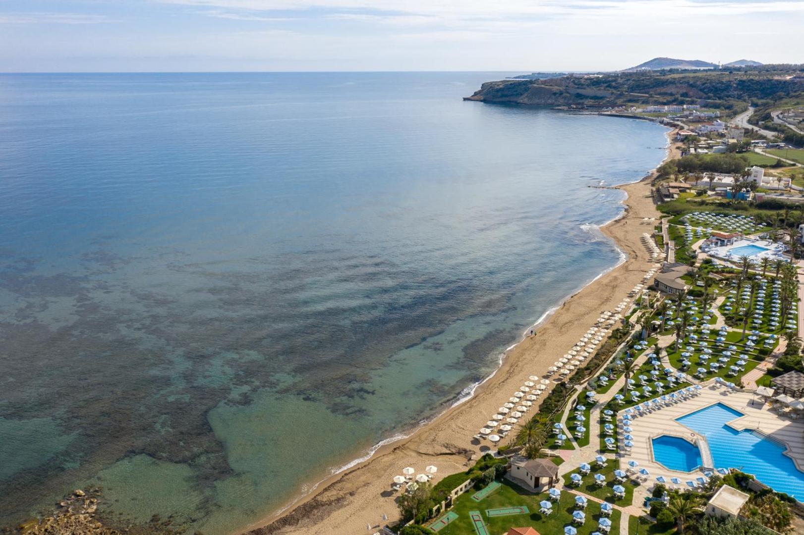 Aerofoto skats uz Creta Star Hotel piekrasti Grieķijā — plaša smilšu pludmale, zila jūra un viesnīcas dārzi ar baseiniem.