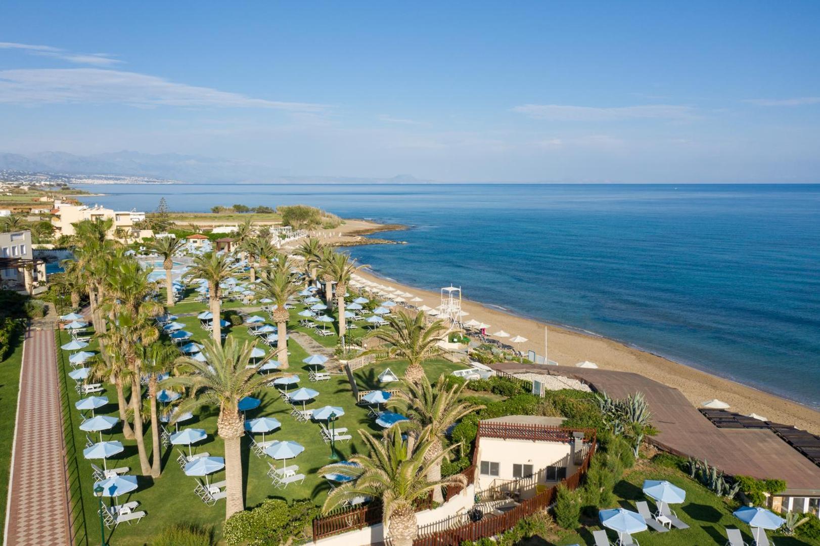 Creta Star Hotel panorāmas skats uz privāto pludmali, palmu dārzu ar saulessargiem un zilo Vidusjūru Krētas piekrastē pie Retimno.