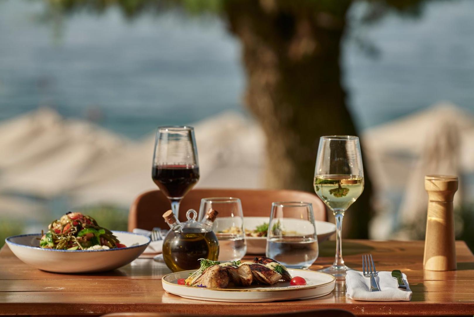 Amira Luxury Resort restorāna klātais galds ar Vidusjūras virtuves ēdieniem un vīna glāzēm piekrastes restorānā Krētā
