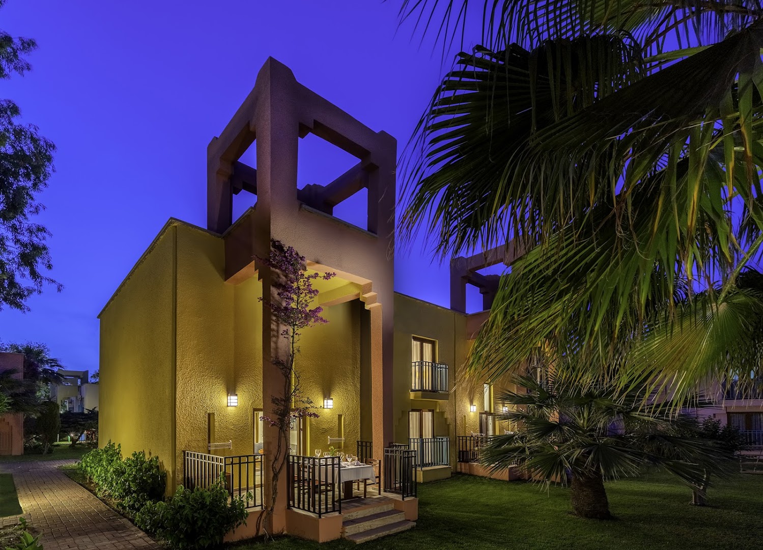 Von Resort Golden Beach divstāvu bungalo ēkas vakarā ar izgaismotām terasēm un palmām dārzā Sides reģionā, Turcijā