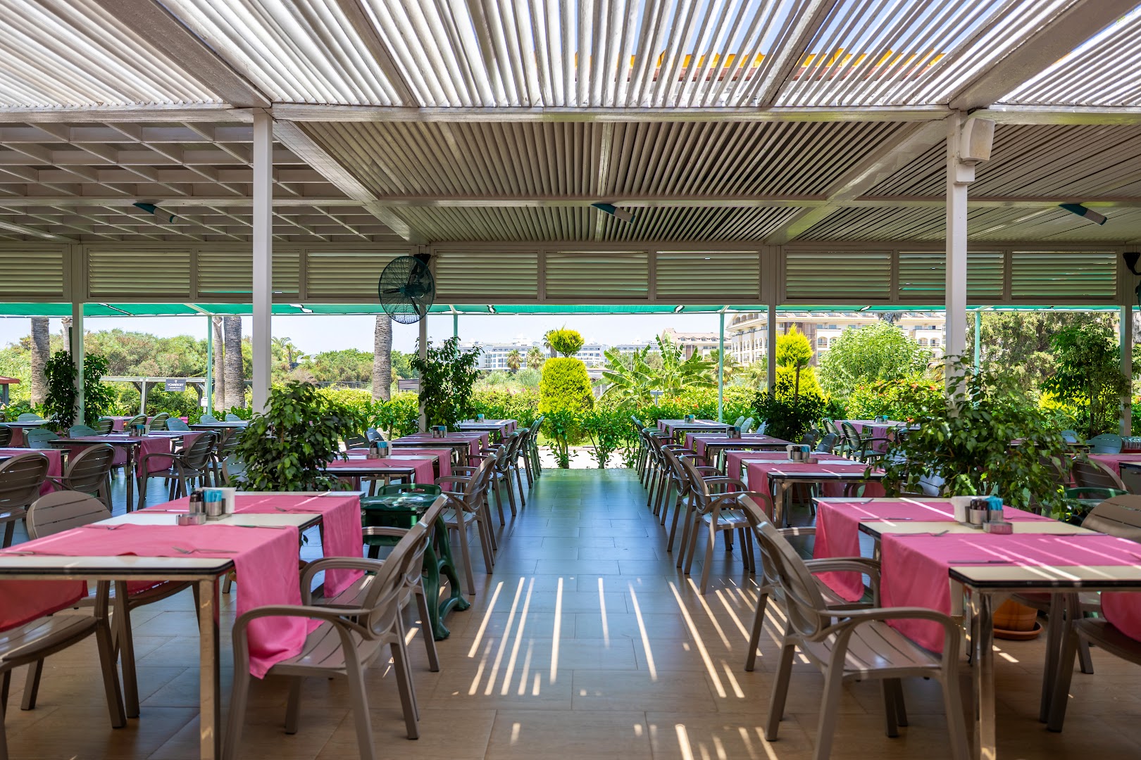 Von Resort Golden Beach plaša āra terase ar galdiem un rozā galdautiem dārza ielokā Sides kūrortā