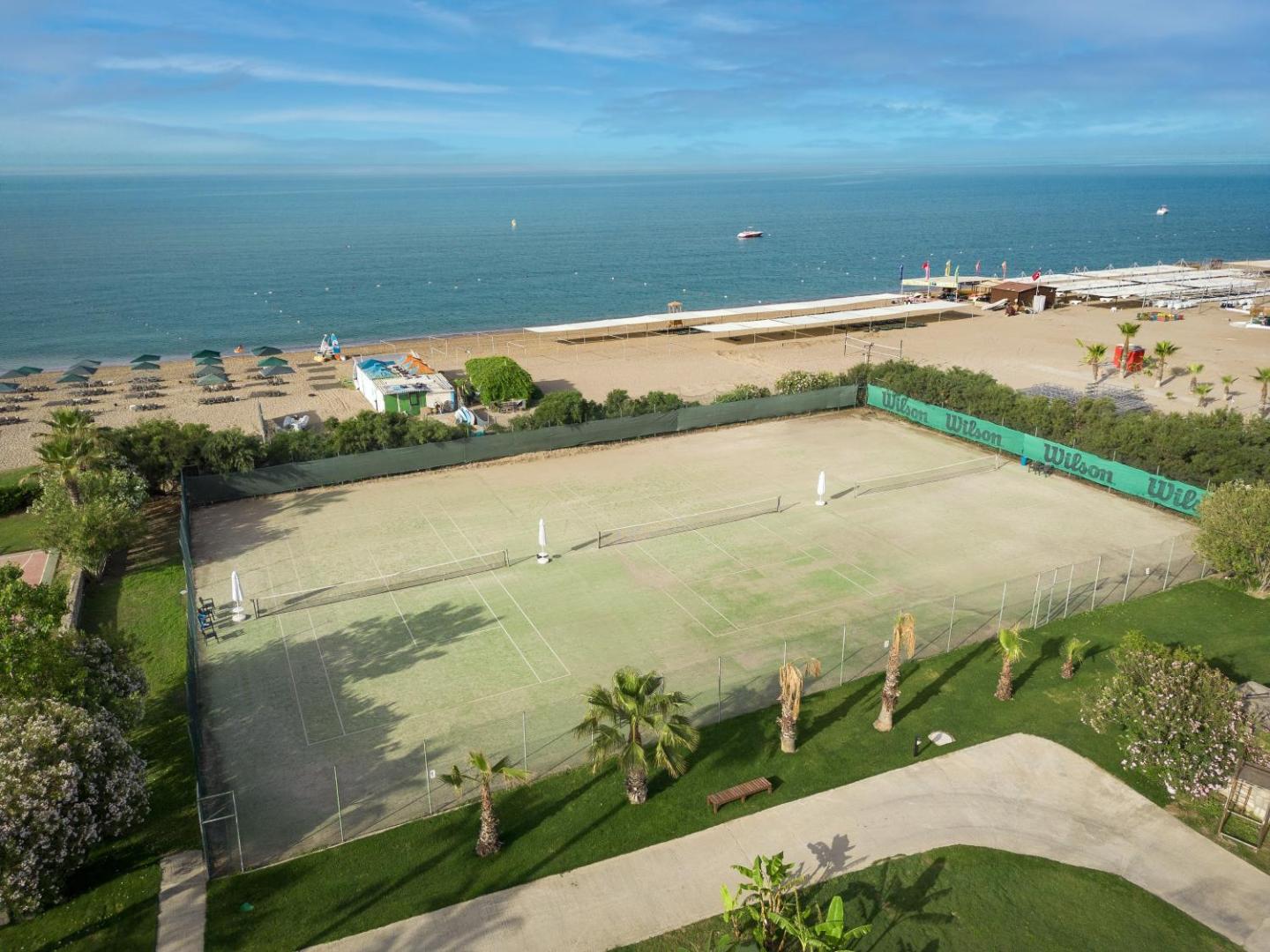 Kaya Side tenisa korti piekrastē blakus smilšu pludmalei — skats no augšas uz sporta zonu un Vidusjūras panorāmu