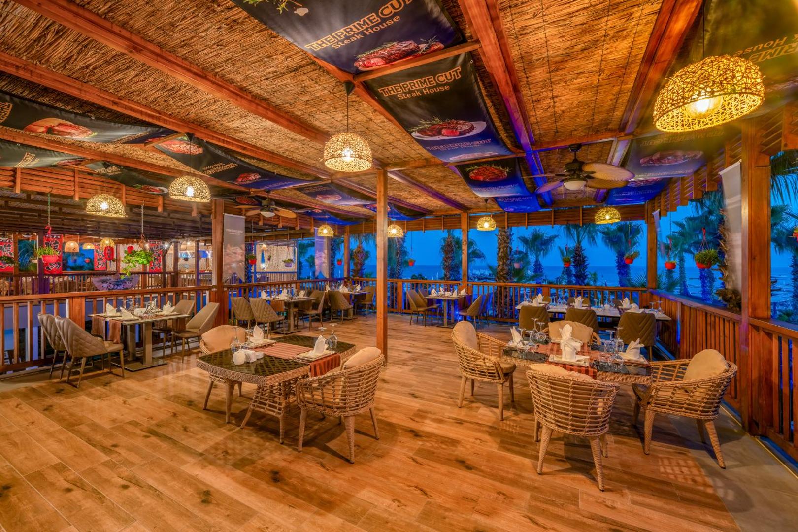 The Prime Cut Steak House restorāns viesnīcā Delphin Diva — elegants interjers ar koka apdari un skatu uz jūru vakarā