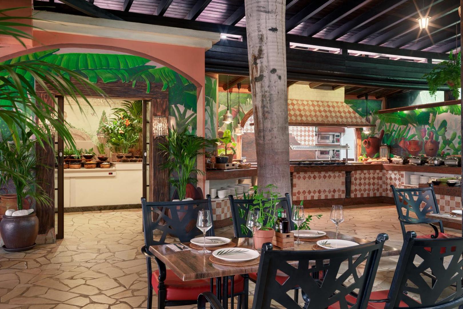 Green Garden Eco Resort restorāna iekštelpas ar atvērto virtuvi, sienu gleznojumiem un elegantiem galdiem