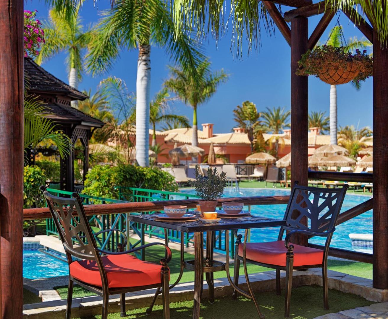 Green Garden Eco Resort āra terase pie baseina ar palmām un saulessargiem Tenerifes dienvidu piekrastē