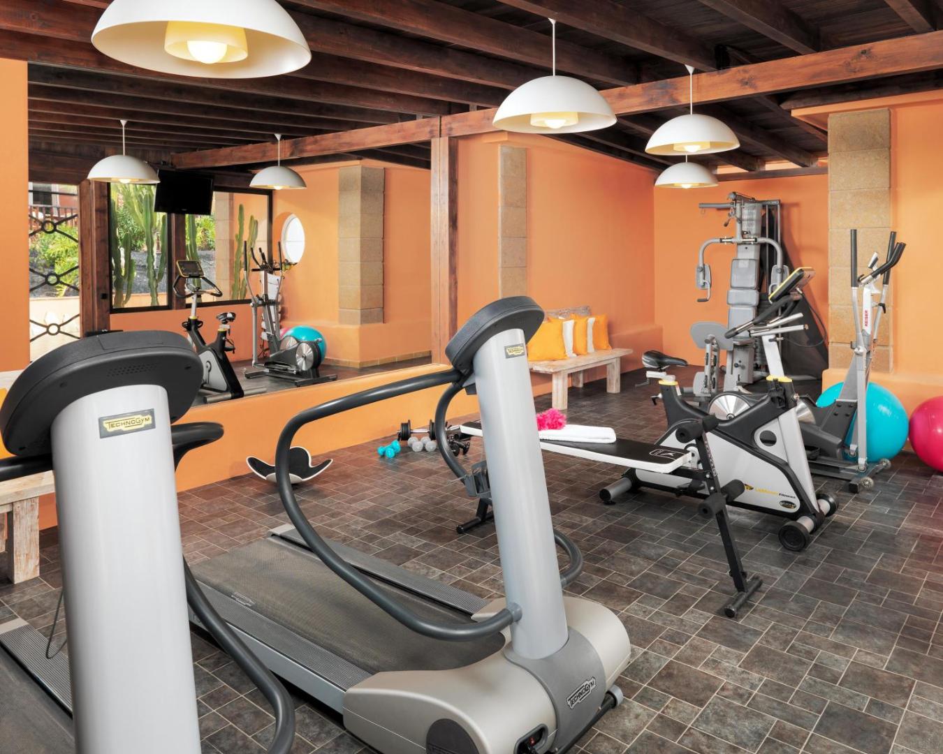 Green Garden Eco Resort fitnesa zāle Tenerifē ar moderniem Technogym skrejceliņiem, velotrenažieriem un brīvajiem svariem gaišā telpā ar koka sijām