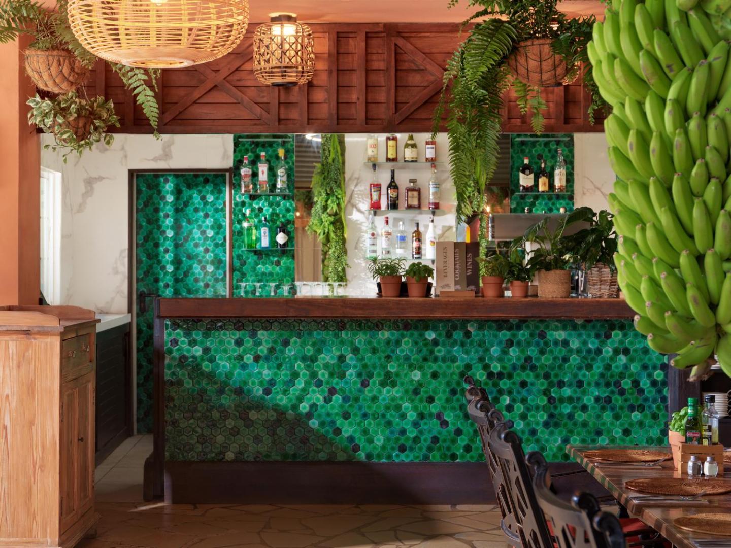 Green Garden Eco Resort bārs ar zaļām mozaīkas flīzēm, koka apdari un svaigiem banānu ķekariem — tropiska stila interjers