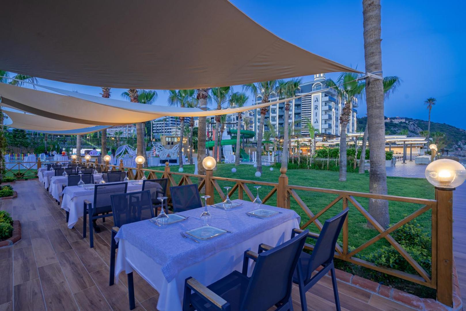 Aria Resort & Spa vakara skats uz viesnīcas ēku, dārzu un āra restorāna zonu zem nojumēm