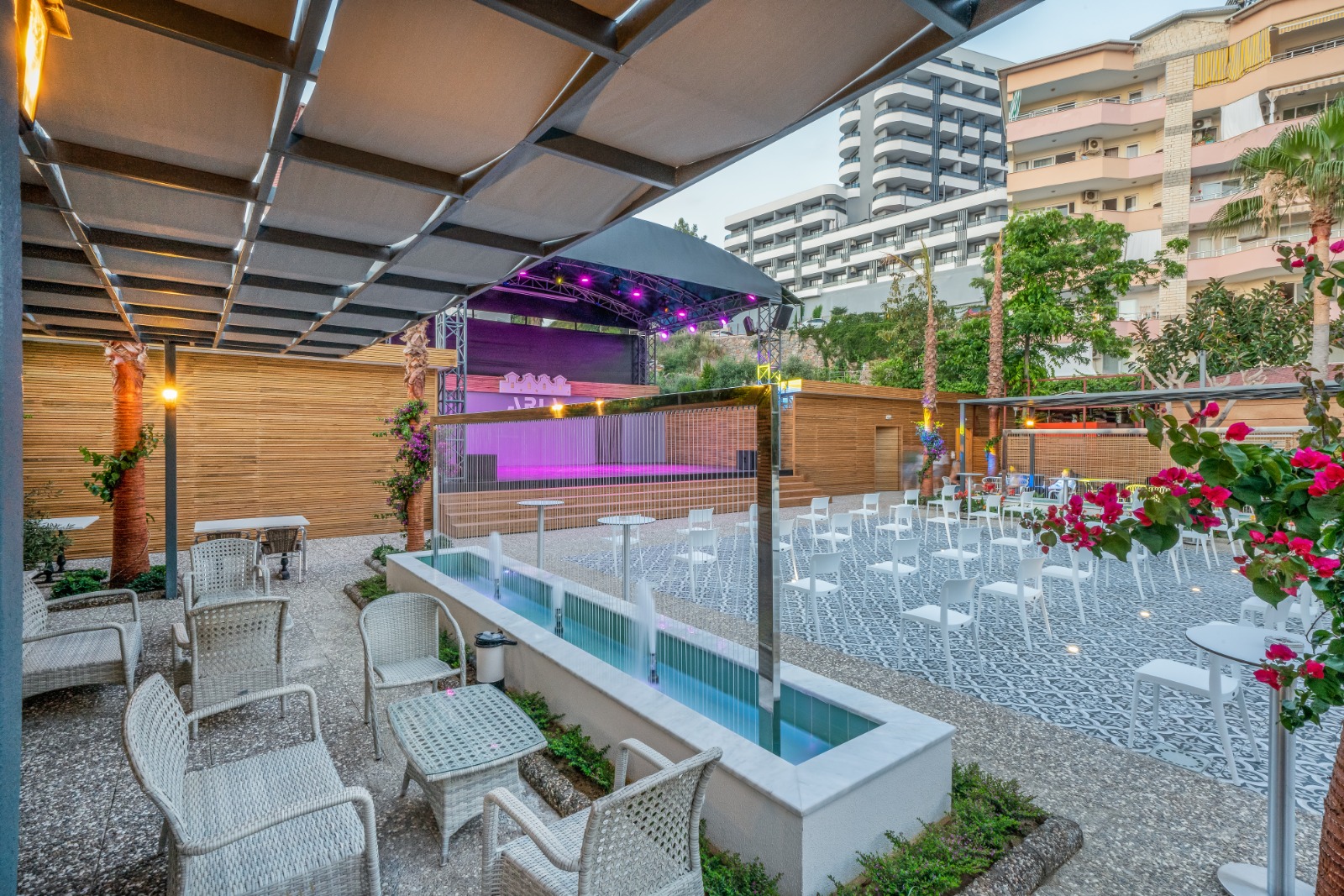 Aria Resort & Spa Hotel vakara pasākumu zona ar strūklaku, pītiem krēsliem un izgaismotu skatuvi Alānijas piekrastē