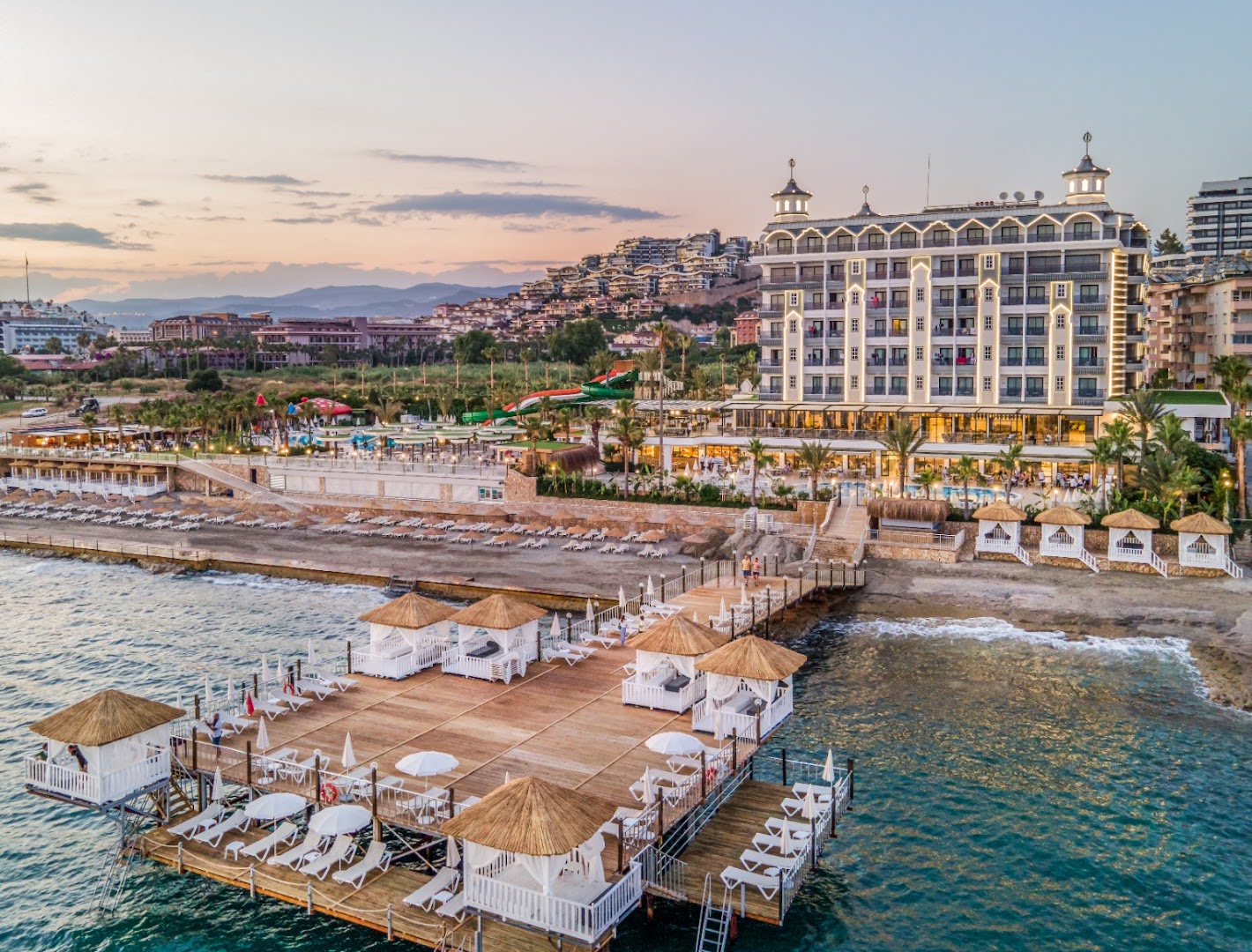 Aria Resort & Spa Hotel koka piestātne ar atpūtas nojumēm un sauļošanās krēsliem saulrieta laikā Alanjas piekrastē
