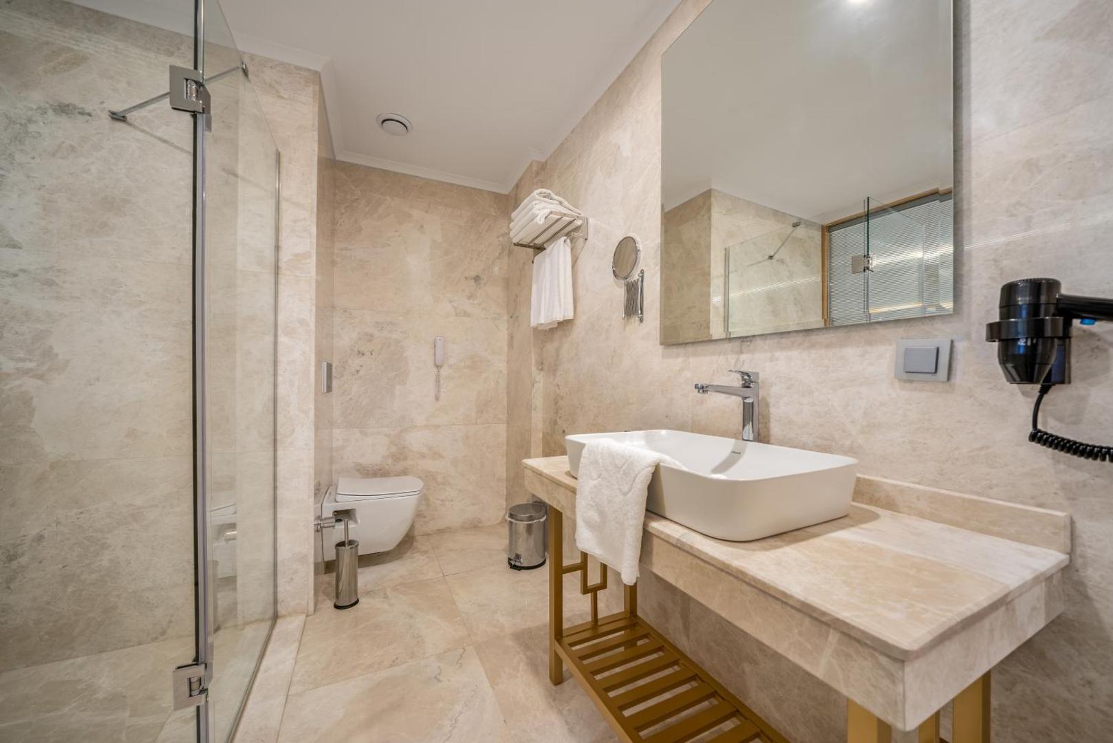 Aria Resort & Spa Hotel moderns numura vannas istabas interjers ar gaišu marmora apdari un dušas kabīni