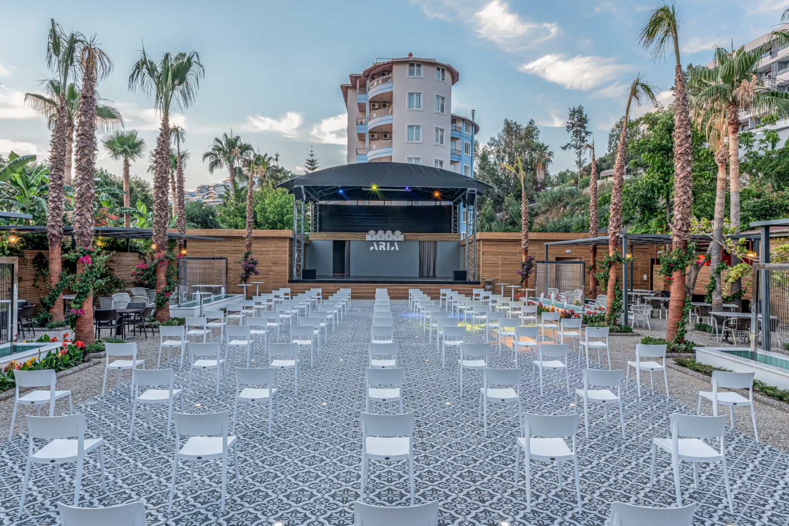 Aria Resort & Spa Hotel amfiteātris un brīvdabas skatuve ar baltiem krēsliem un palmām pasākumu norisei
