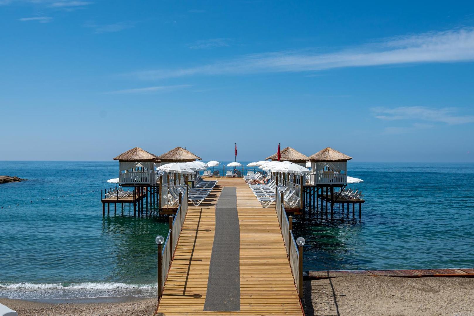 Aria Resort & Spa koka mols ar sauļošanās krēsliem un saulessargiem Alānijā, Turcijā — skats uz dzidro Vidusjūru