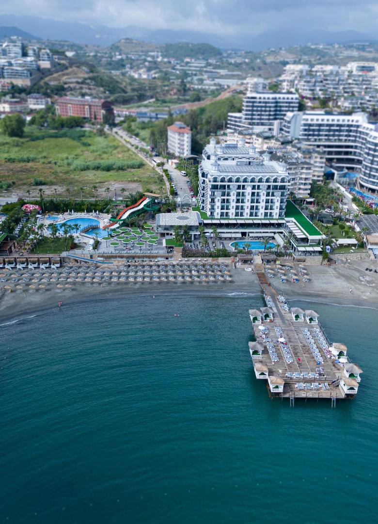 Aria Resort & Spa Hotel aerofoto skats uz viesnīcas galveno ēku, pludmali un apkārtējo kalnu ainavu Turcijā