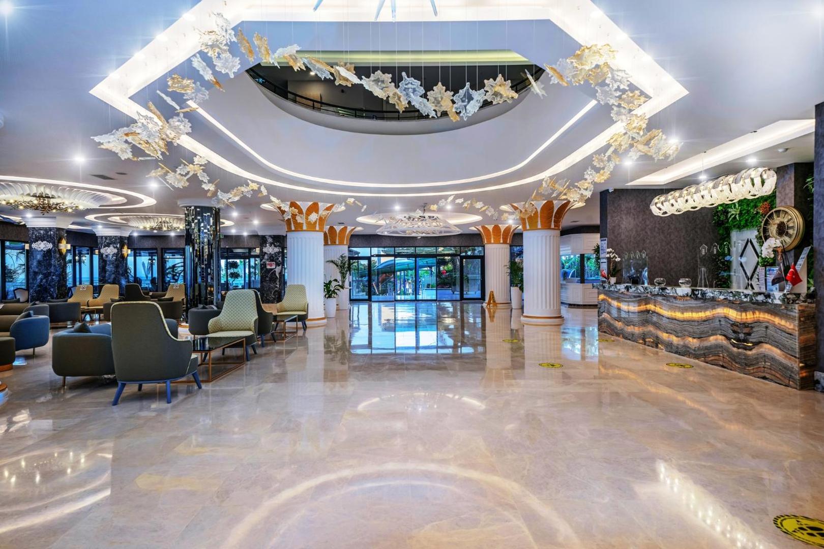 Aria Resort & Spa Hotel plašais un modernais lobby vestibils ar marmora grīdām, dekoratīvām kolonnām un dizaina apgaismojumu Alānijas reģionā
