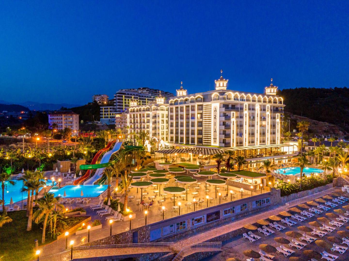 Aria Resort & Spa Hotel apgaismota ēka vakarā Alanjā ar āra baseiniem, ūdens slidkalniņiem un atpūtas zonu piekrastē