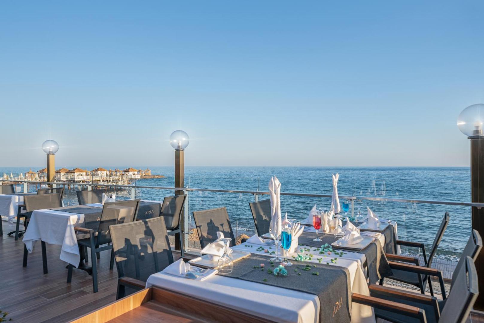 Aria Resort & Spa āra restorāna terase ar klātiem galdiem un skatu uz Vidusjūru saulrietā