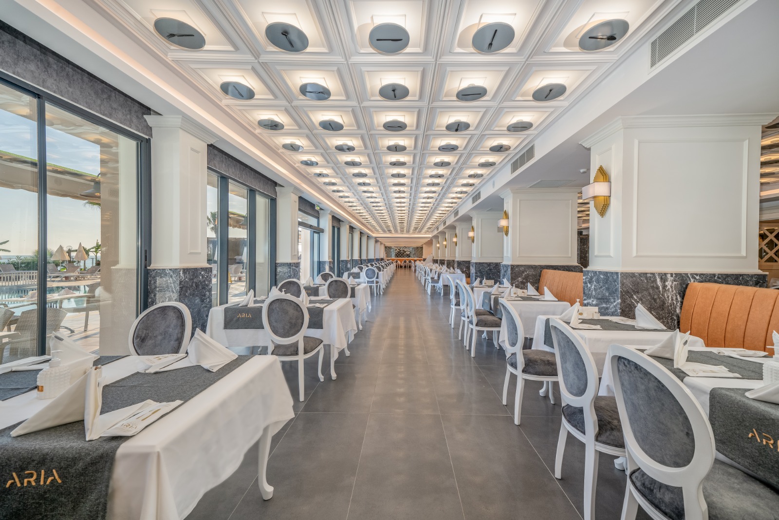 Aria Resort & Spa galvenā restorāna iekštelpas ar modernu interjeru, baltiem galdiem un dekoratīviem griestiem