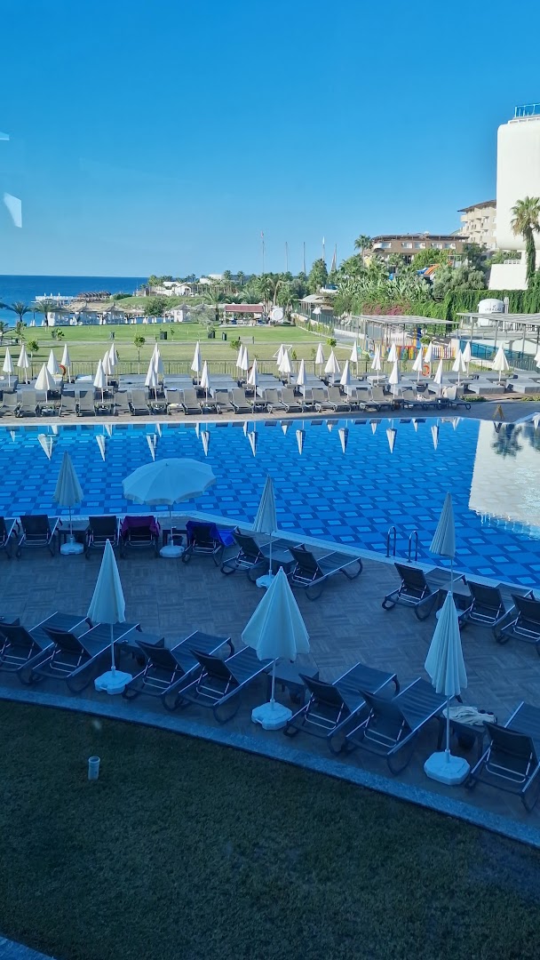 Skats no Lonicera Premium terases uz baseina zonu un Vidusjūru tālumā — sakopta zāliena teritorija ar saulessargiem un atpūtas krēsliem
